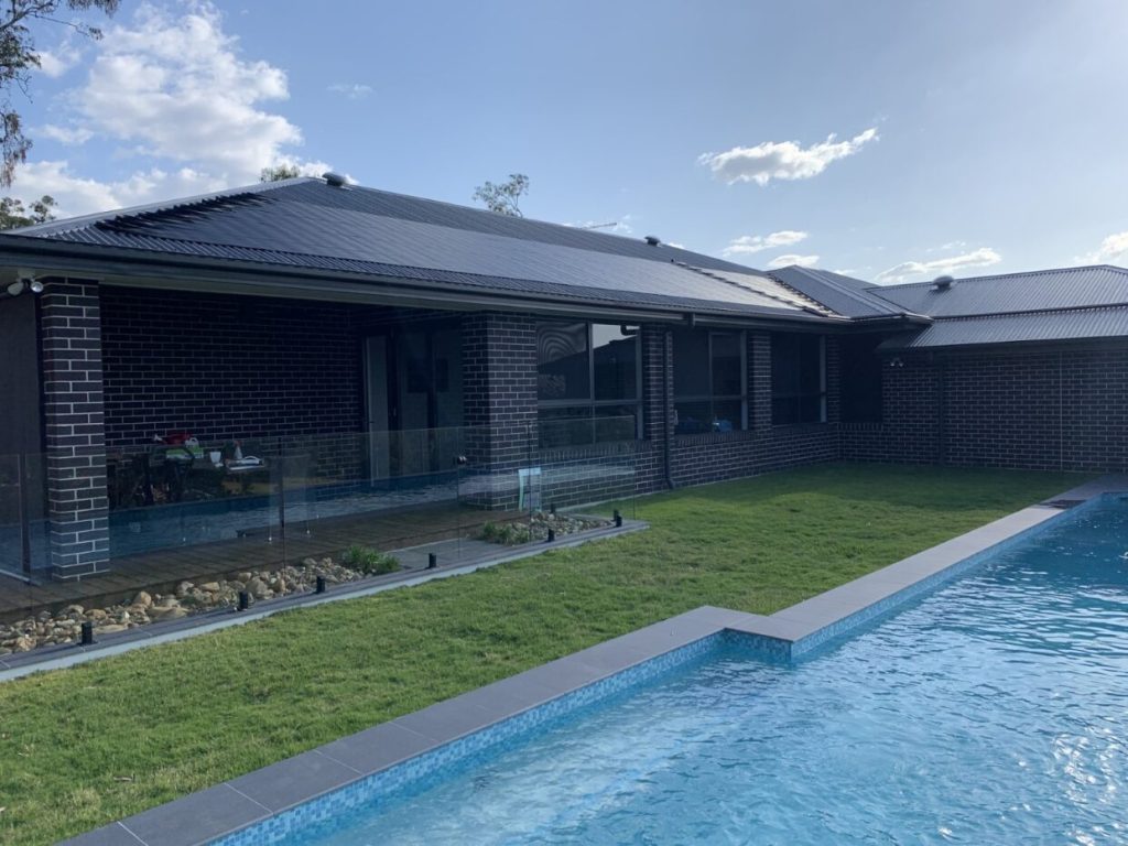Black solar pool heating panels covering a roof beside an in-ground pool