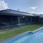 Black solar pool heating panels covering a roof beside an in-ground pool