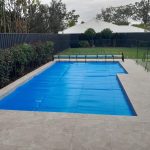 Blue solar pool cover fitted over a rectangular in-ground pool