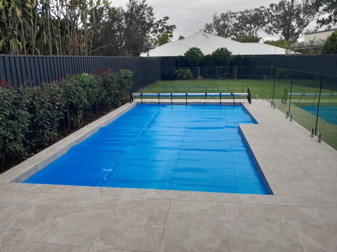 Blue solar pool cover fitted over a rectangular in-ground pool