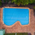 Aerial view of a curved pool fitted with a blue Ultra Silverback solar pool cover
