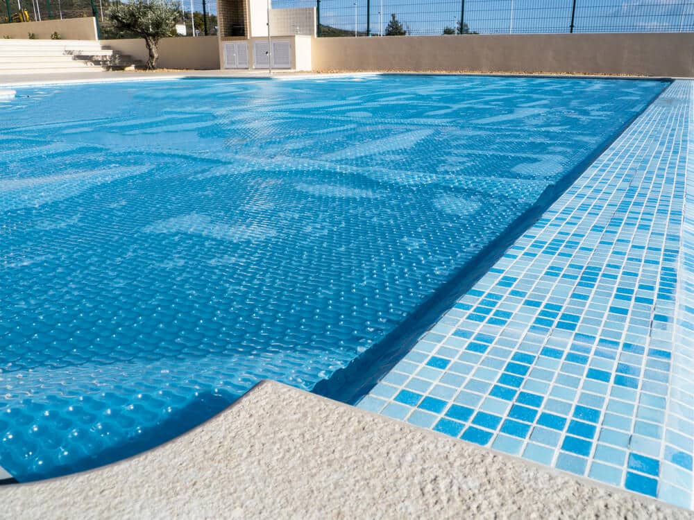 Swimming pool covered with a blue solar thermal pool cover