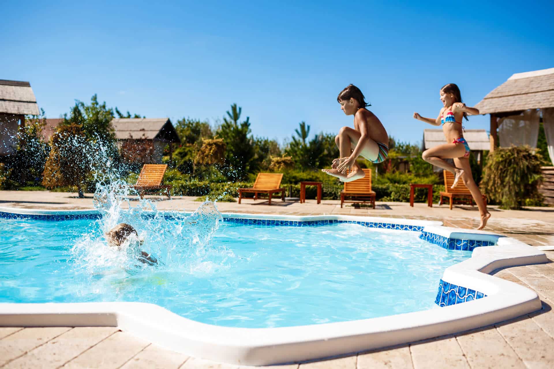 Two children jumping and splashing into an outdoor swimming pool