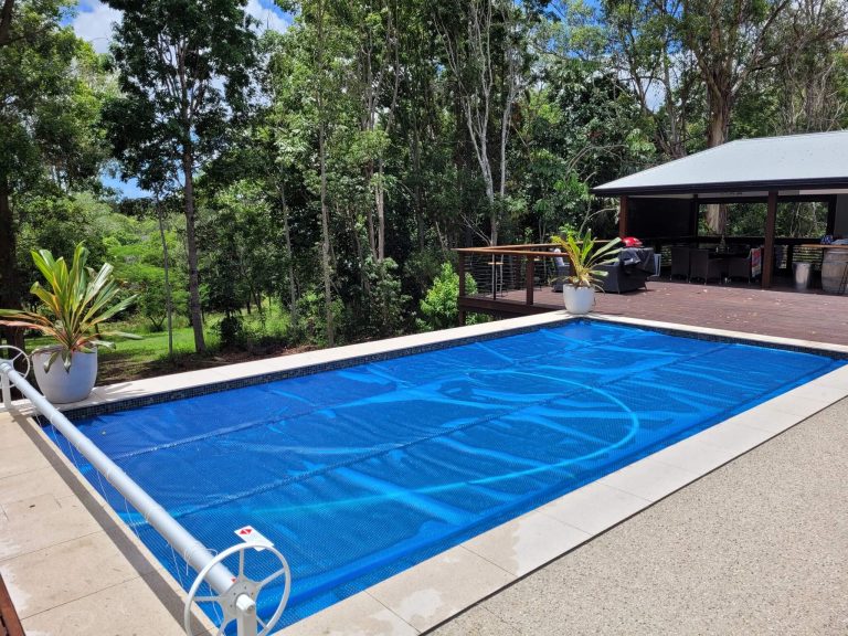 Blue solar pool blanket covering a rectangular pool with roller beside timber deck
