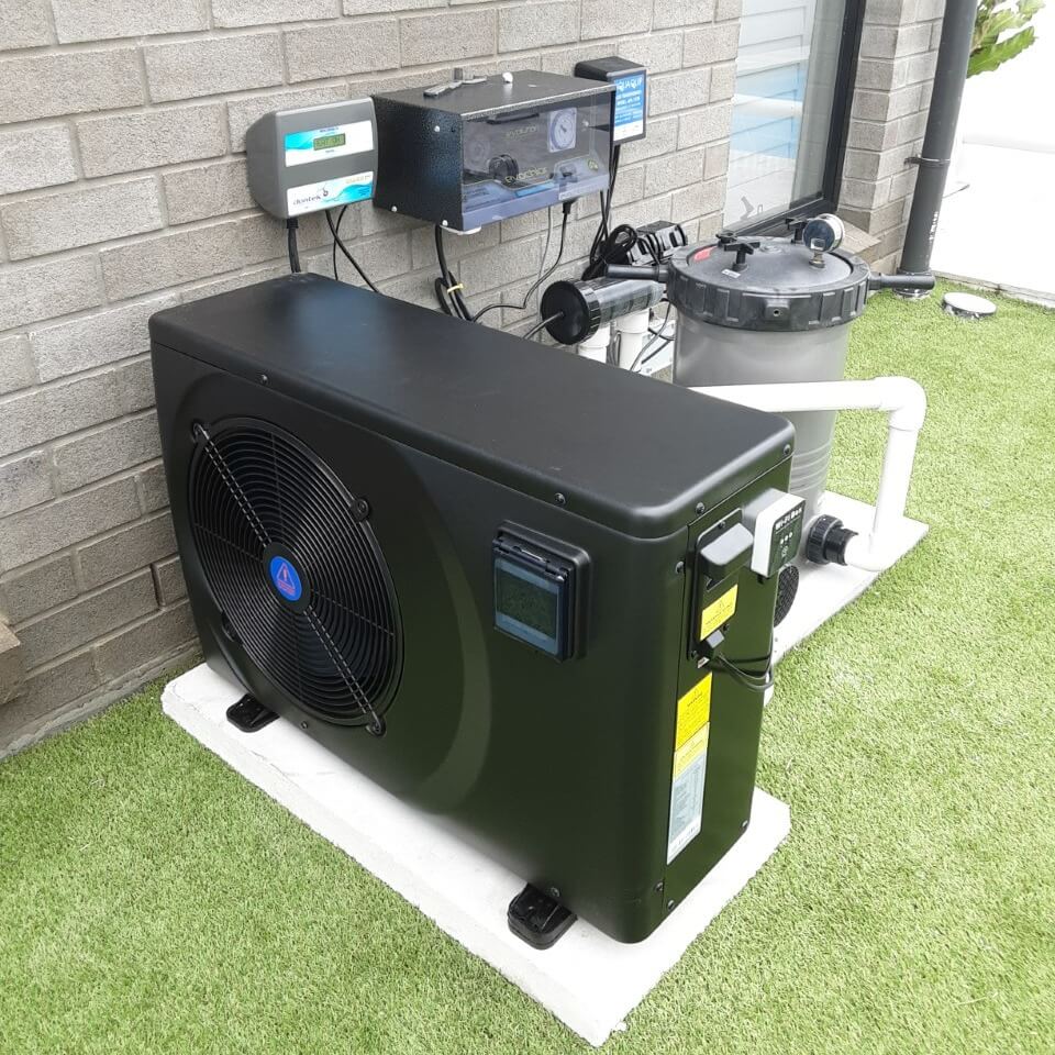 Black pool heat pump unit installed outdoors on artificial turf - How Much Does Pool Heat Pump Repair Cost?