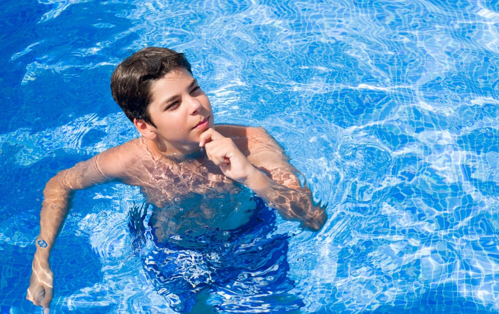 Teenage boy swimming and looking up in a bright blue pool - How does a pool heat pump work? Will it work for me?