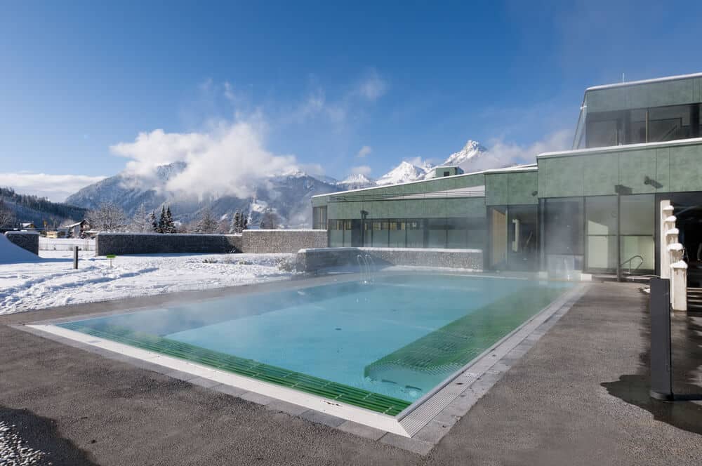 Steaming heated outdoor pool with snowy mountains in the background - Is pool heating worth it in winter?