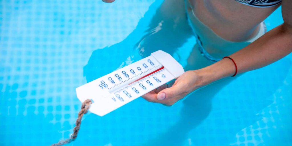 Hand holding a floating pool thermometer in blue water - Is pool heating worth it in Queensland?